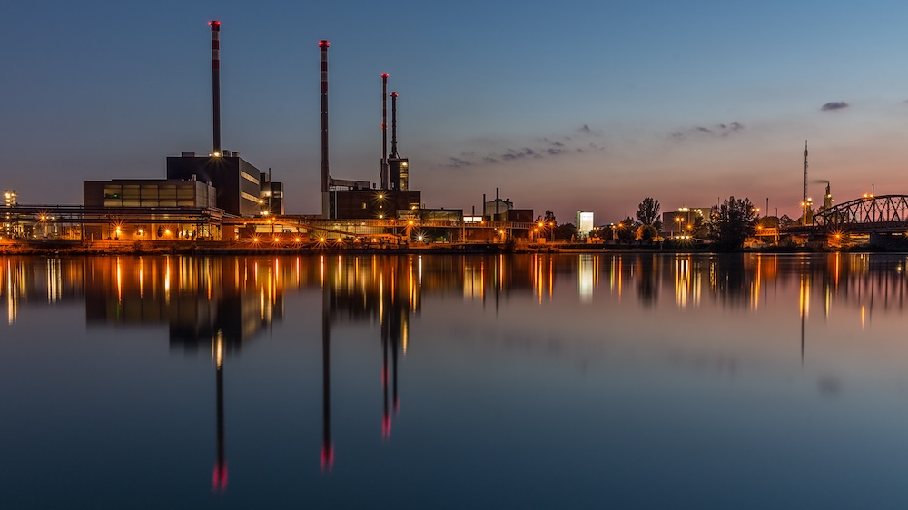 A factory, its lights reflecting in the water of the Danube at dawn