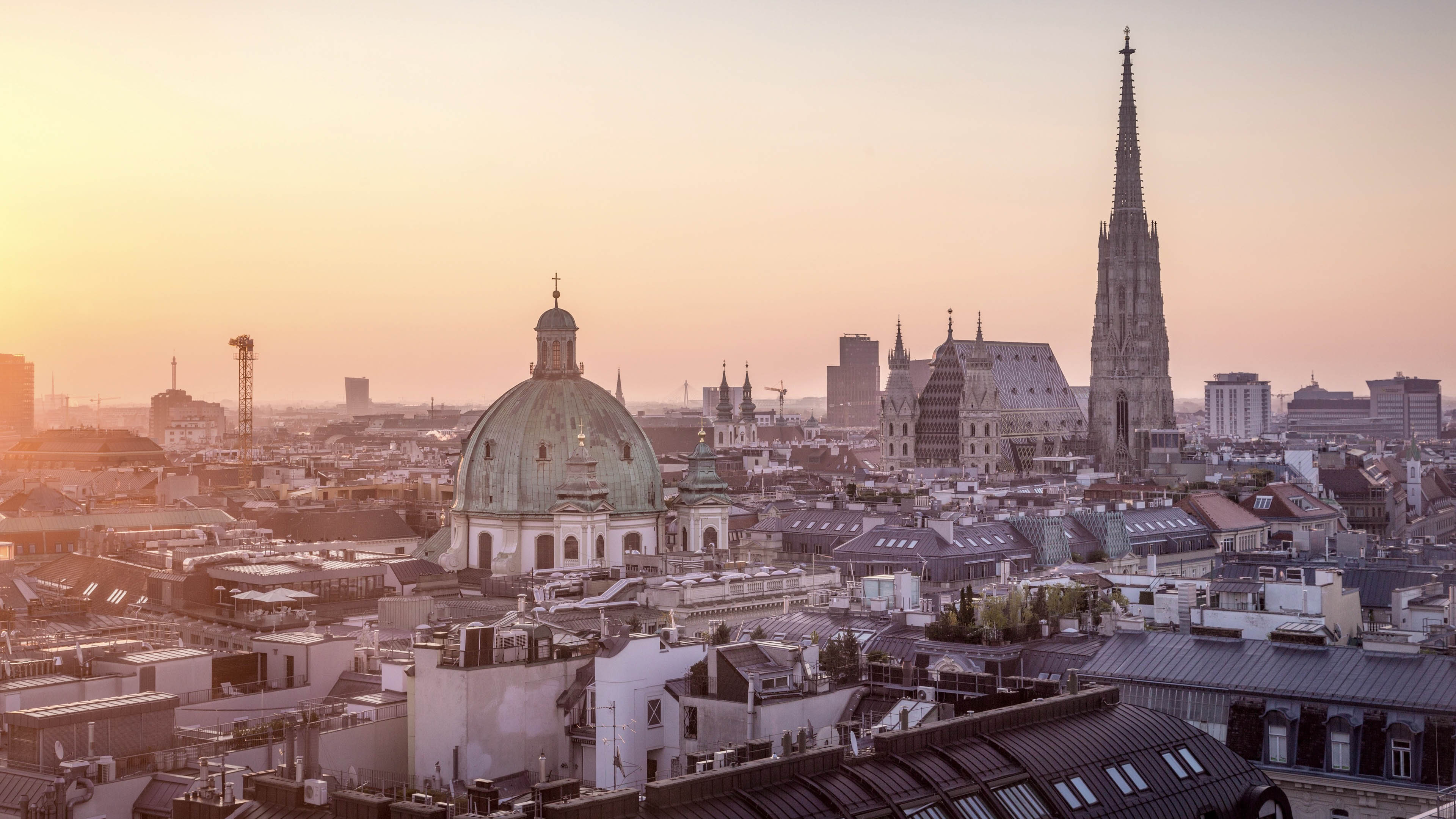 The sun is setting over the rooftops of Vienna, with St. Stephens Cathedral and Peterskirche