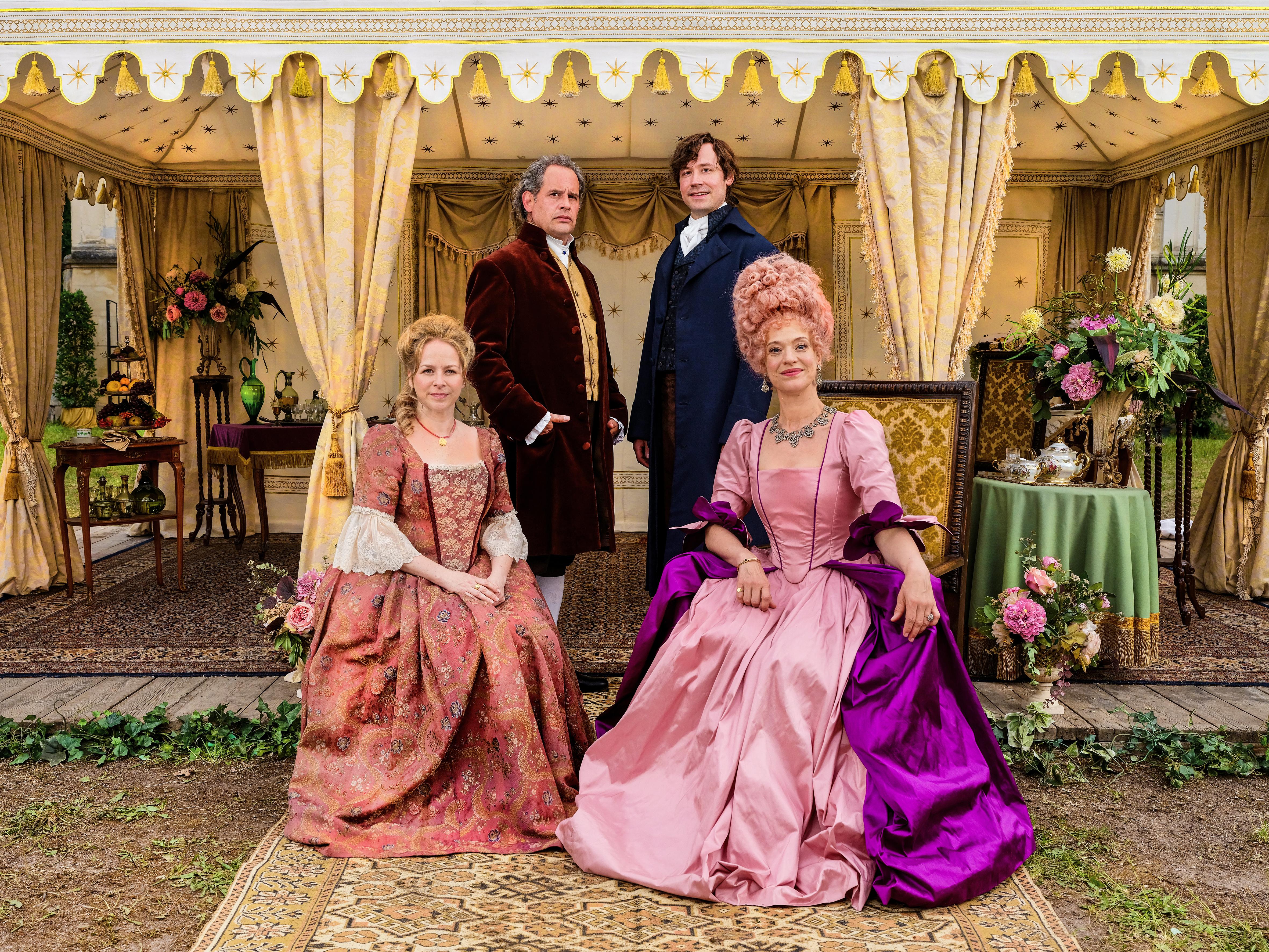 Actresses Jasmin Schwiers and Heike Makatsch sit in front of actors Moritz Bleibtreu and David Kross. They are dressed in fancy clothes from the late 18th century and look into the camera