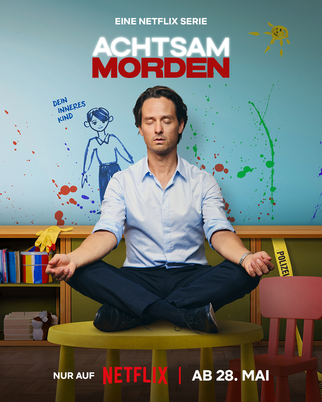 A man (main character Björn Diemel) meditates on a kids chair, behind him is paint smeared on the wall and a painting of his inner child
