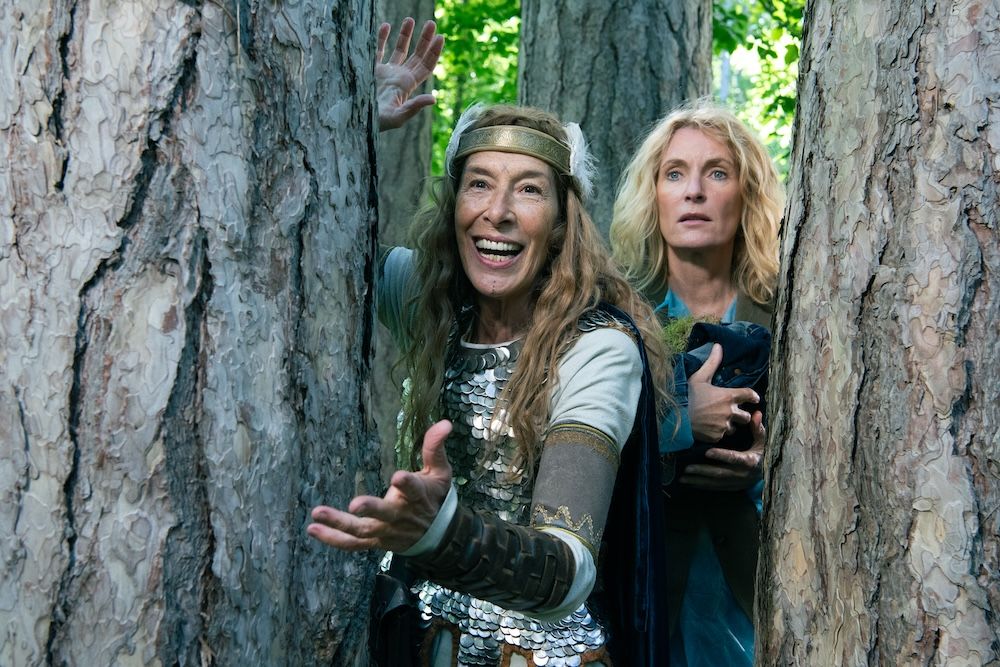 Valkyrie Wolkenthrut and Prof. Frieda Hofstätter are looking to the camera, hiding between two trees. Wolkenthrut is looking ecstatic, while Frieda is looking concerned